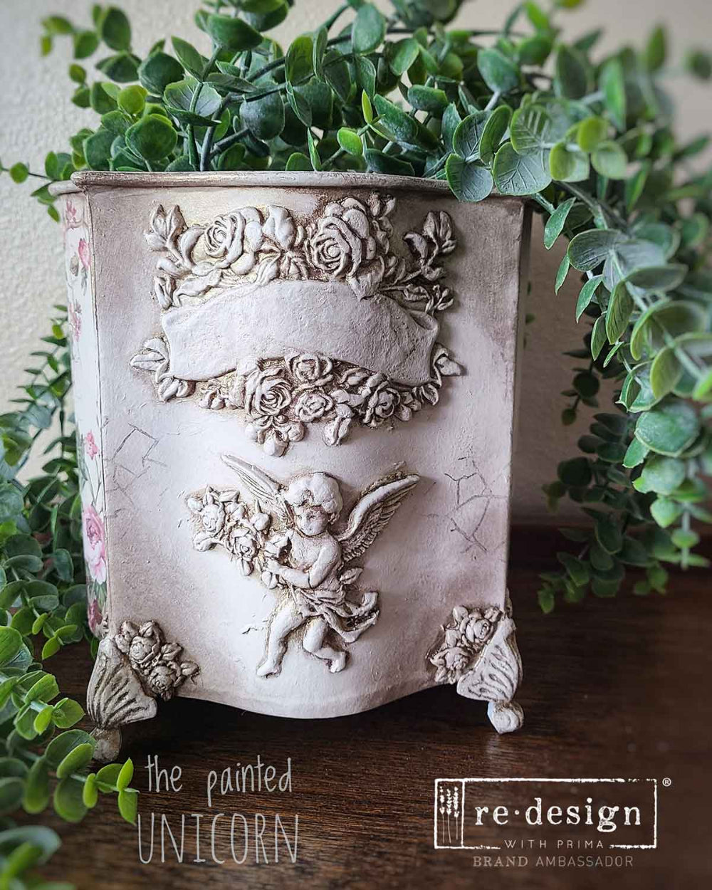 Decorative planter with floral and angel design, featuring 'the painted unicorn' and 're-design' logos.