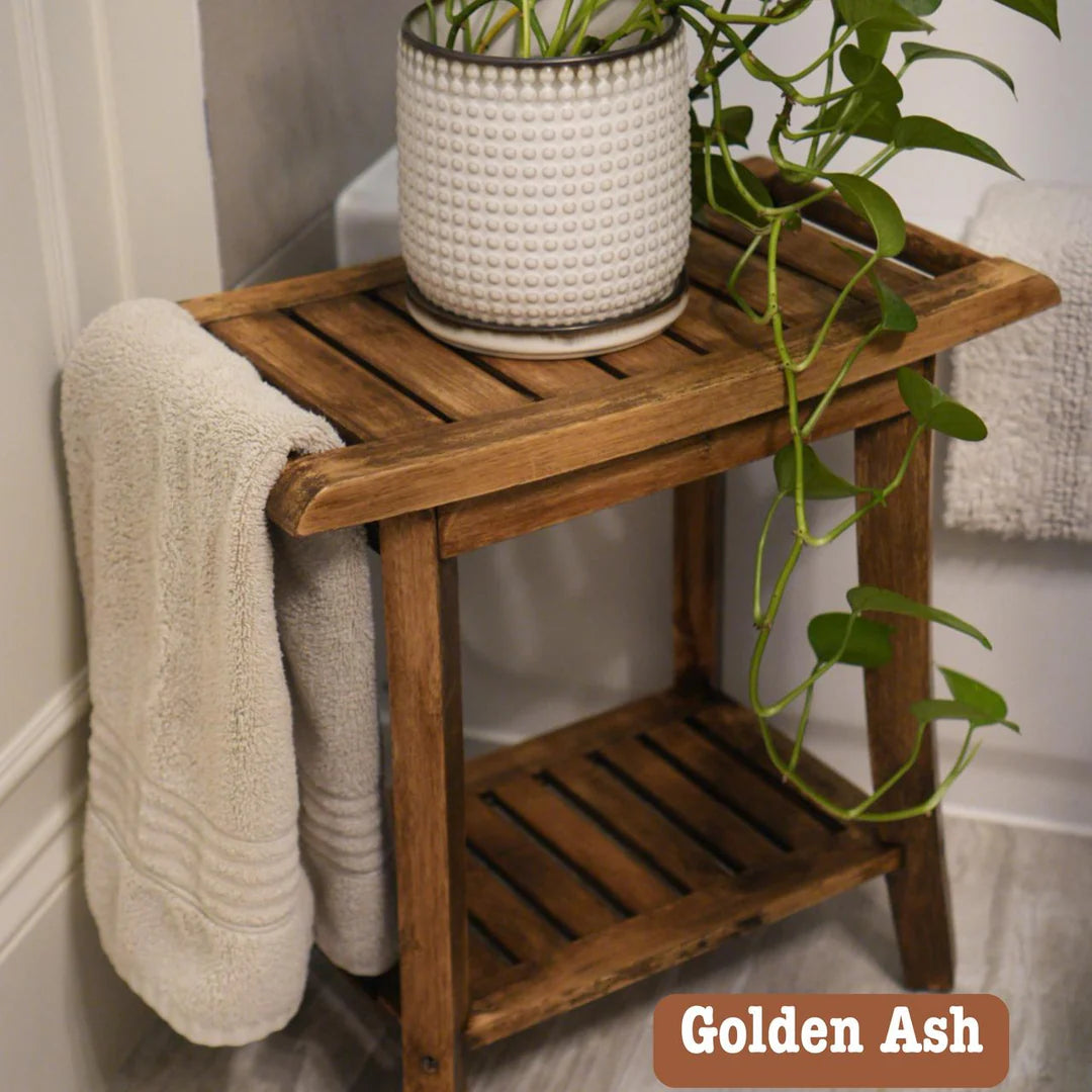 A rustic wooden bathroom side table in Golden Ash, styled with a white textured planter and trailing green plant, with a cream towel draped over the side, set against a neutral bathroom background.