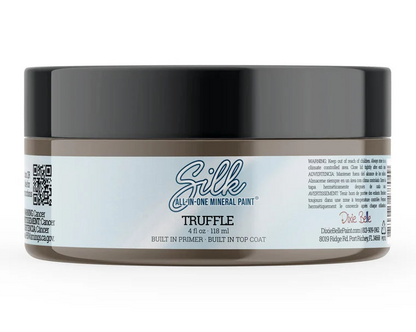 A jar of Silk Truffle Mineral Paint on a clean white background. The product features a dark gray lid, a brown container body, and a white label with blue and black text.