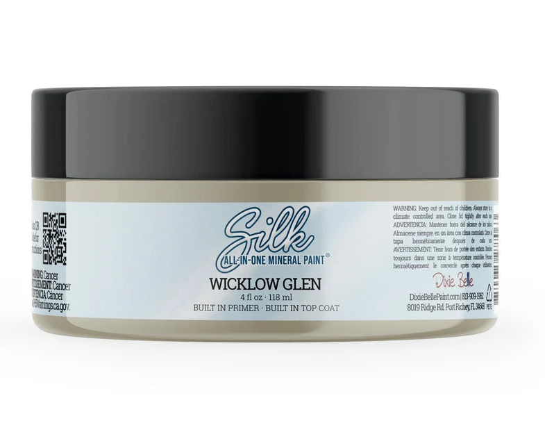 A jar of Silk Oxford Fog hair primer on a plain white background. The product is in a clear plastic jar showing a light gray primer inside, with a black screw-on lid and a white label featuring the brand name 'Silk' in blue script.