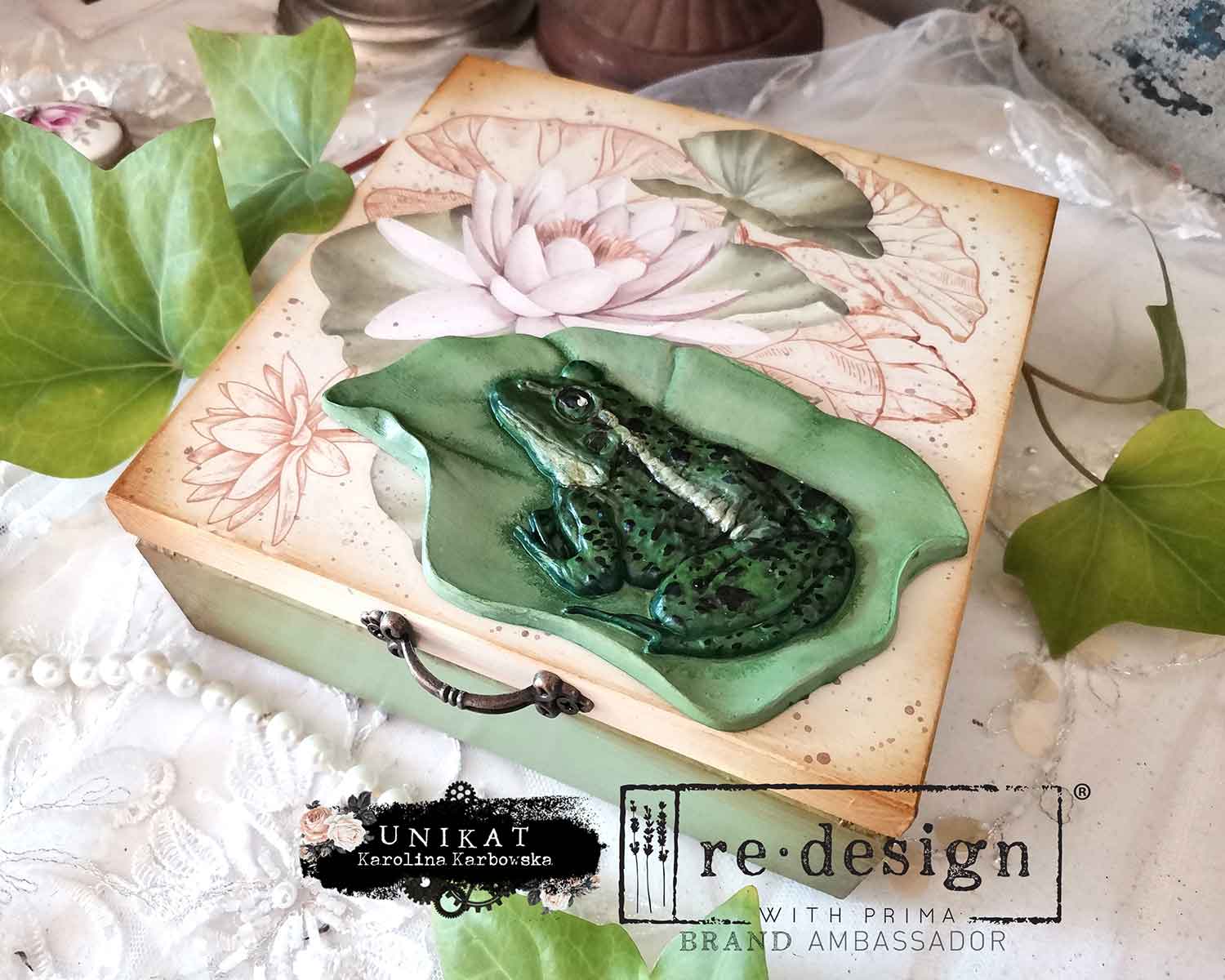 Decorative box with a green frog design on a textured surface, featuring 'Unikat' and 're·design' branding.