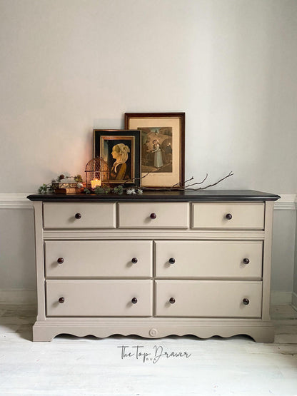 Gray dresser with black top against a white wall, featuring decorative items on top.