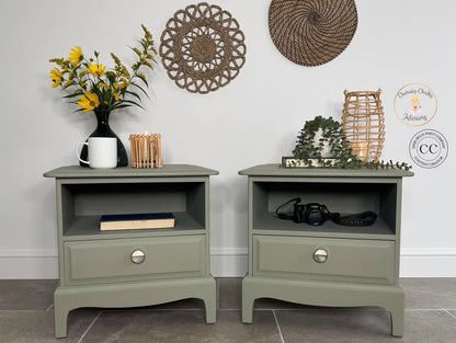 Two olive green bedside tables shown in a styled room setting with home decor, including a vase of yellow flowers, woven wall art, and decorative baskets. A circular logo for 'Carmen Clarke Furniture' is visible on the right side.