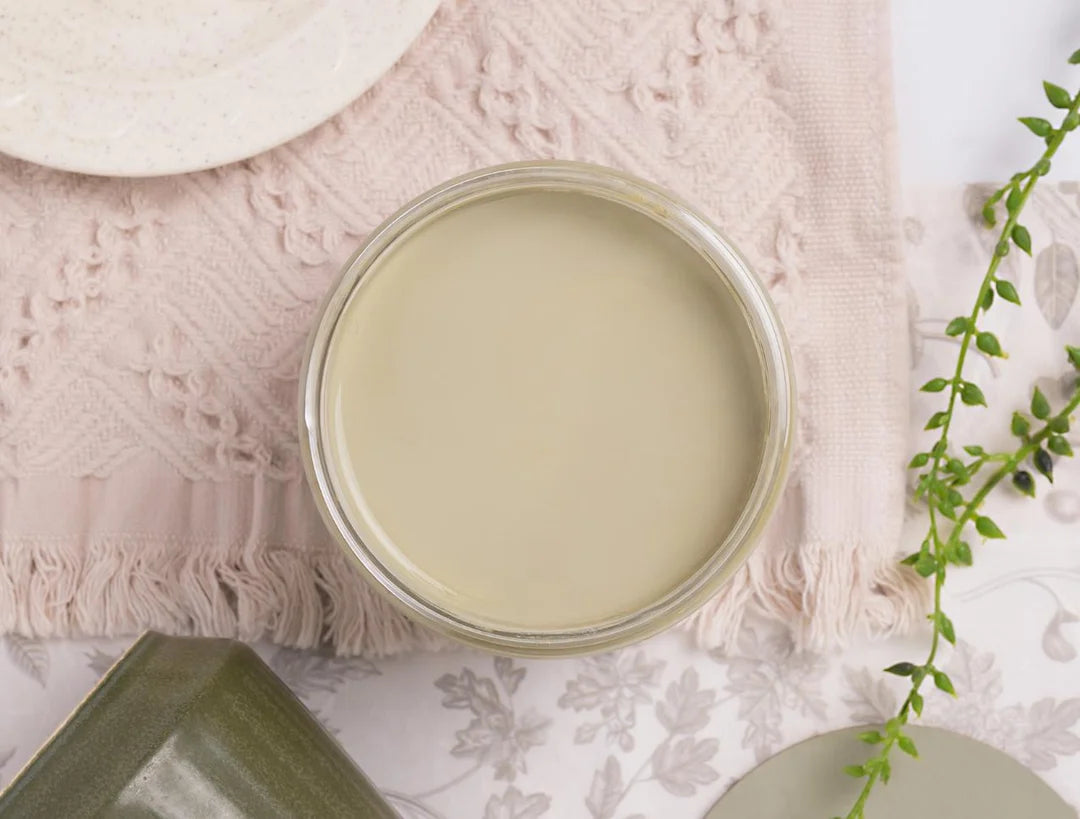 An open round glass jar filled with a pale creamy olive green dixie belle paint